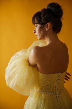 Profile portrait of a beautiful middle-aged woman in a yellow dress, her hair pulled up against a yellow background.