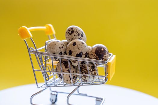Happy Easter background. Easter quail eggs in the shopping cart on bright yellow paper. Festive concept.