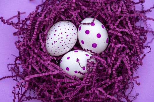 Colorful eggs in purple artificial bird's nest isolated on purple background. Easter concept