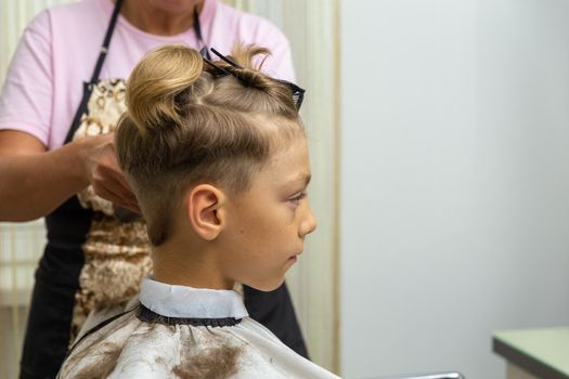 Nice european boy getting hairstyle in barbershop. Hairdresser makes a hairstyle for a boy.