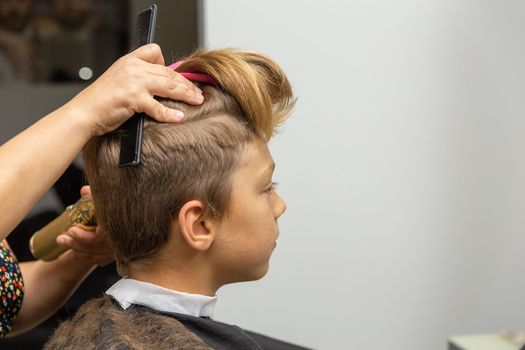 Nice european boy getting hairstyle in barbershop. Hairdresser makes a hairstyle for a boy.