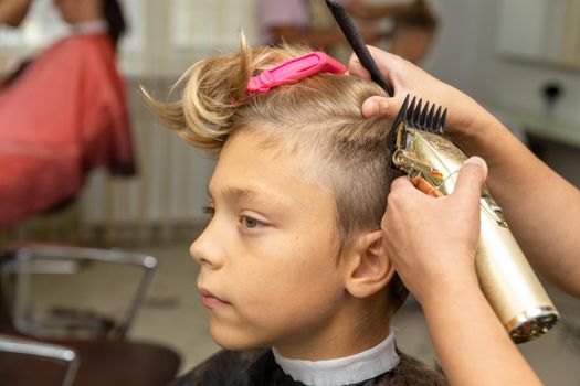 Nice european boy getting hairstyle in barbershop. Hairdresser makes a hairstyle for a boy.