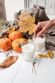 Hello fall. Cozy warm image. High angle view autumn composition with sweaters and candles, white candle mockup design. Woman hand lighting candles