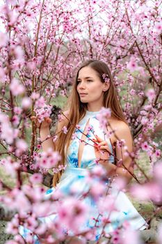 Young beautiful woman in blue dress and long hair is enjoying with blossoming peach trees.