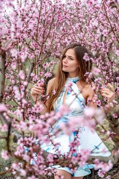 Young beautiful woman in blue dress and long hair is enjoying with blossoming peach trees.