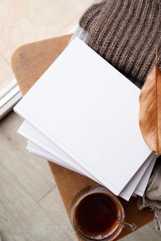 Back to school. Cozy autumn. Study and education concept. Stack of white blank books with autumn leaves and cup of hot tea on old wooden chair, mockup design