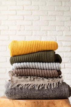 Hello fall. Cozy warm image. Stack of autumn warm sweaters on modern coffee table, white brick wall background