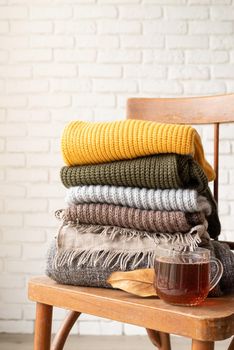 Hello fall. Cozy warm image. Stack of autumn warm sweaters on old wooden chair, white brick wall background