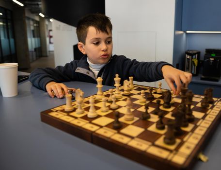 Caucasian elementary age boy thinking on chess move, developing strategy while playing chess. Intelligent hobby, logic development, leisure activity, board games for kids development and entertainment