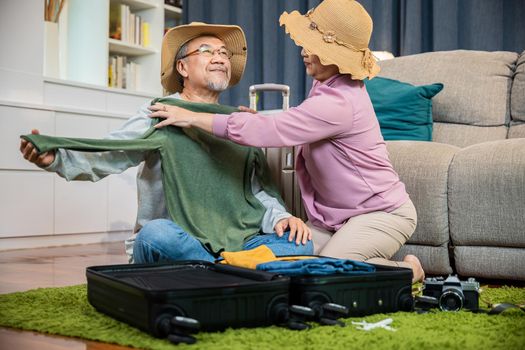 Asian couple old senior marry retired couple prepare luggage suitcase arranging for travel, Romantic retired couple packing clothes travel bag suitcase together on floor at home interior living room
