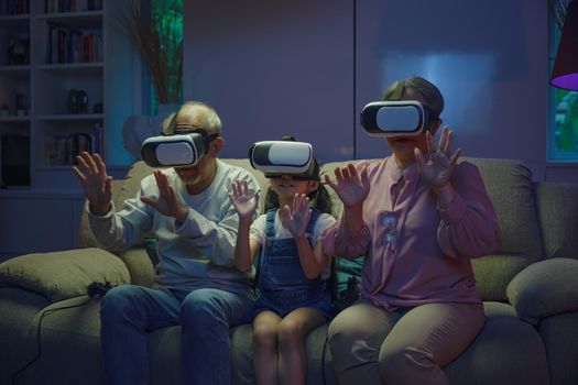 Asian granddaughter and grandparents playing together exciting interesting video games using virtual reality headsets living room at home, elderly with child play VR video game, family entertainment