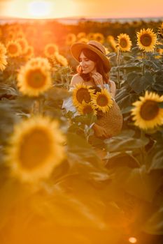 A girl in a hat on a beautiful field of sunflowers against the sky in the evening light of a summer sunset. Sunbeams through the flower field. Natural background