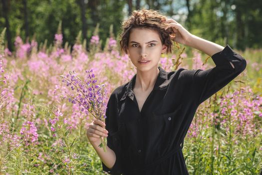 Young woman with a bouquet of lupines in her hand against the background of blooming Ivan-tea A meadow with purple flowers in summer.