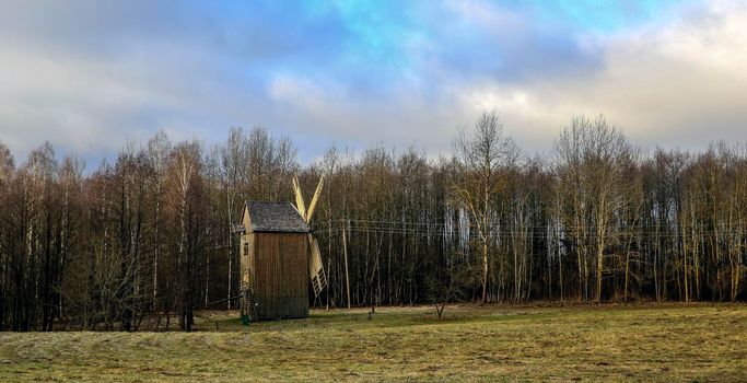 Landscape view of the old mill in the field against the background of the autumn forest.