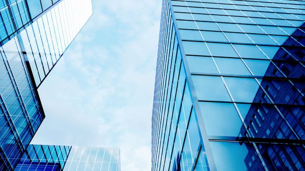 Glass buildings business concept. The glass facade of a skyscraper with a mirror reflection of sky windows. Bright sunny day with sunbeams in the blue sky. Modern buildings background. 3d Rendering