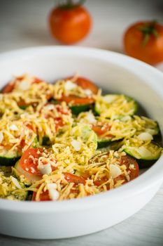raw zucchini and tomatoes sliced with cheese, prepared for baking in a ceramic dish.