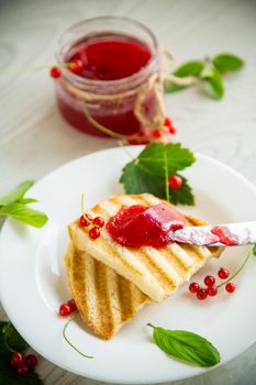 fried bread croutons for breakfast with redcurrant jam in a plate with berries on a wooden table.