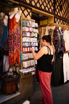 Happy female tourist smiling and looking at camera while choosing accessories on rack on clothes market