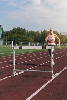 Young woman athlete runnner running hurdles at the stadium outdoors