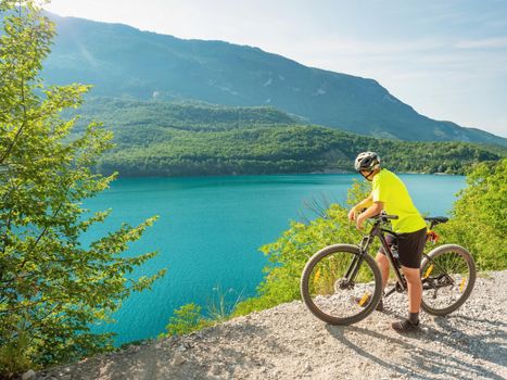 Young biker looking over Molveno lake from gravel trail round around. Amazing summer holiday in Dolomites Alps, Italy.