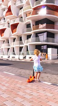 Dubai, UAE - 04.02.2021 - Little girl riding a scooter in front of Binghatti pearls residential building.