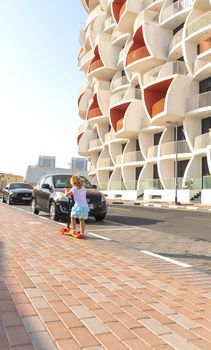 Dubai, UAE - 04.02.2021 - Little girl riding a scooter in front of Binghatti pearls residential building.