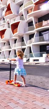 Dubai, UAE - 04.02.2021 - Little girl riding a scooter in front of Binghatti pearls residential building.