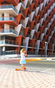 Dubai, UAE - 04.02.2021 - Little girl riding a scooter in front of Binghatti crystals residential building.