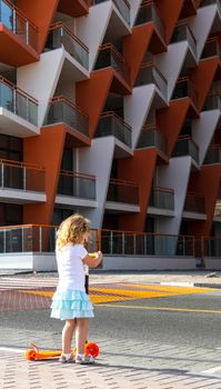 Dubai, UAE - 04.02.2021 - Little girl riding a scooter in front of Binghatti crystals residential building.