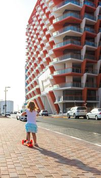 Dubai, UAE - 04.02.2021 - Little girl riding a scooter in front of Binghatti crystals residential building.
