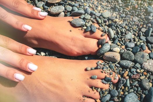 Hands and feet on the background of a rocky beach of sea pebbles.