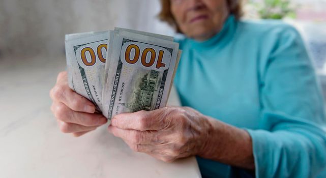 Close-up of an elderly woman's hands holding money in 100 dollar bills, compensation.