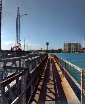 Rusty Metal walkway attached to road along waterway in San Juan, Puerto Rico with construction in the distance.