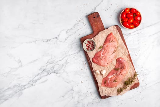 two raw veal escalope on the old wooden cutting board, ready to cook, marbre background, top view, copy space