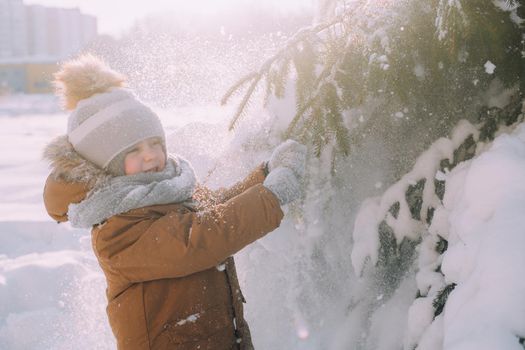 The kid shakes a branch with snow . Winter nature. An article about winter. Winter clothing