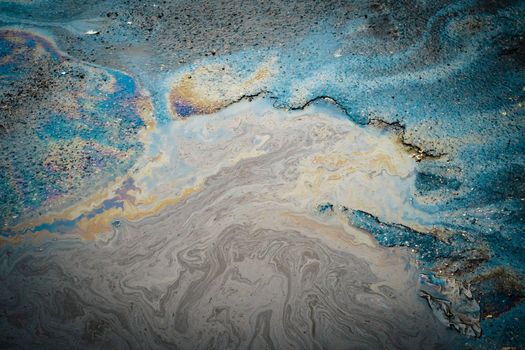 Multi-colored poisonous spots of spilled gasoline on wet asphalt. Environmental pollution concept