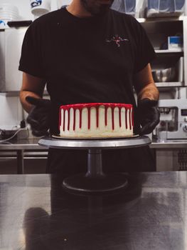 hand pof chef making for icing a red drip cake in the professional kitchen lab