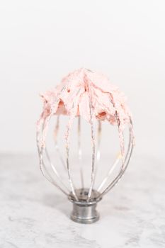 Whisk from the stang-along kitchen mixer filled with strawberry buttercream frosting.