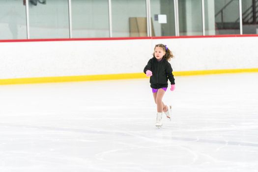 Little girl practicing figure skating on an indoor ice skating rink.