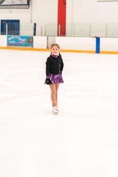 Little girl practicing figure skating on indoor ice skating rink.