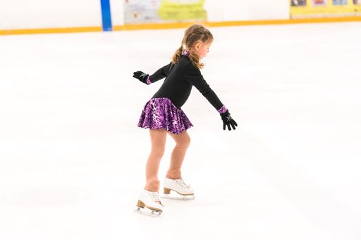 Little girl practicing figure skating on indoor ice skating rink.