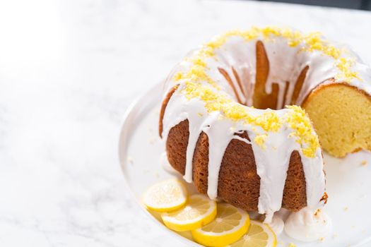 Sliced lemon bundt cake decorated with lemon zest on a cake stand.