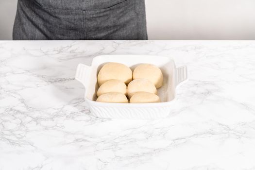 Rising dough in a white ceramic dish to prepare dinner rolls.