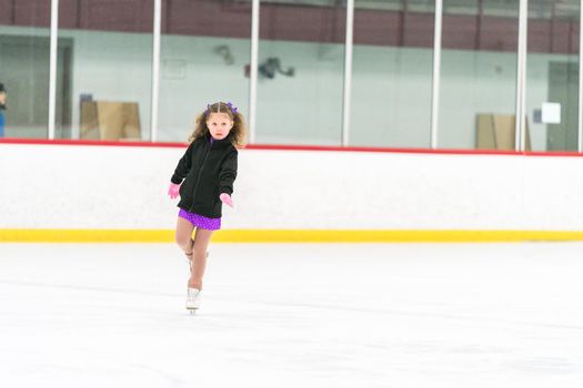 Little girl practicing figure skating on an indoor ice skating rink.