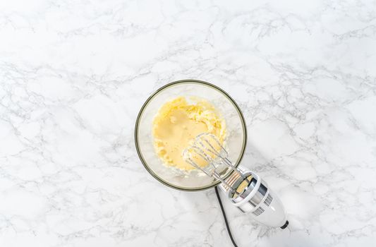 Flat lay. Mixing ingredients with a hand mixer in a large mixing bowl to bake mini vanilla cupcakes with ombre pink buttercream frosting.