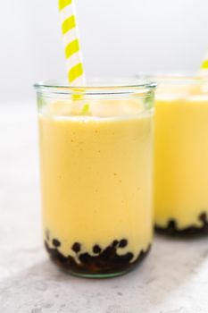 Freshly made mango boba smoothie in a drinking glass with a paper straw.