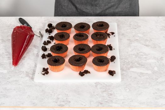 Filling freshly baked chocolate cupcakes with strawberry filling.