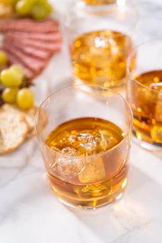 Scotch on the rocks in whiskey glass on a white marble surface.