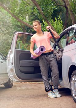 Yoga time. a beautiful young woman carrying a yoga mat while getting out of her car