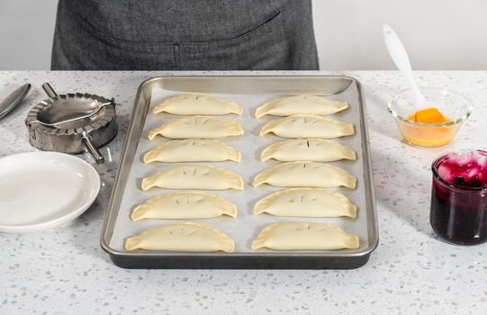 Brushing uncooked empanadas with blueberries with egg wash.